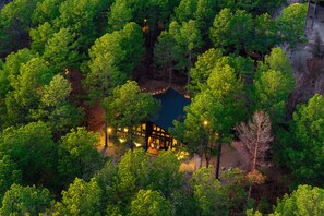 A secluded cabin surrounded by dense forest, with a small pond in the center. - Private & Fun Packed | 3 Kings + Bunk | Hot Tub (Broken Bow)