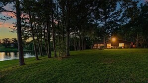Uma casa com gramado bem cuidado e árvores, situada perto de um corpo d'água.