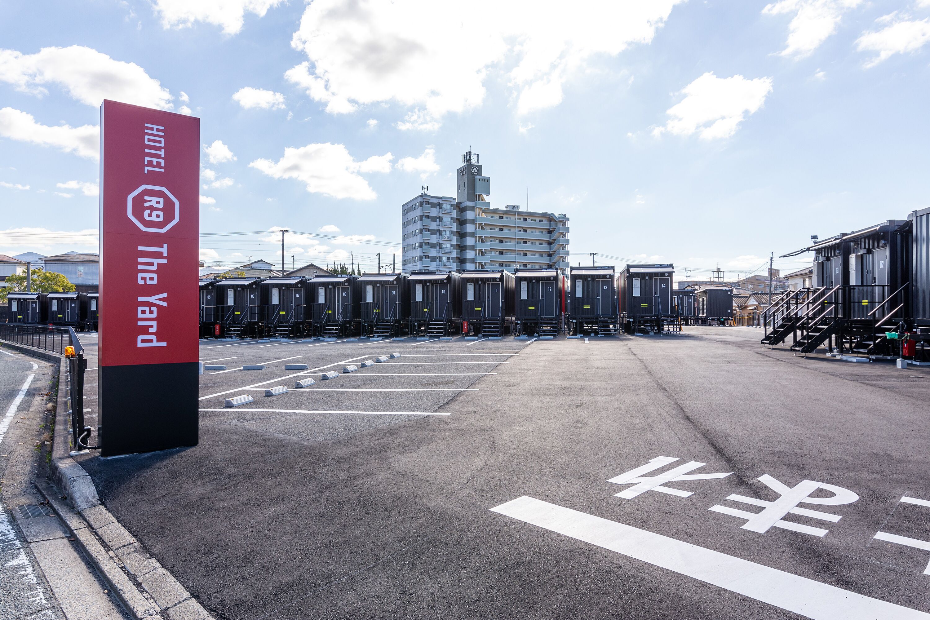 A hotel sign with a red and black design, a parking lot with marked spaces, and a building in the background.