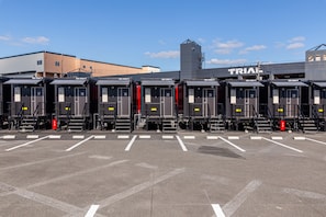 Ein Parkplatz mit mehreren Zugwagen, nummeriert von 17 bis 23, und ein Gebäude mit der Aufschrift 'TRIAL' im Hintergrund.