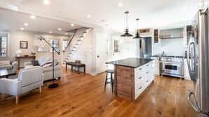 A spacious living area with a wooden floor, a kitchen with modern appliances, and a staircase leading to another level. - Sunsets On Blue Hill, Newly Renovated Farmhouse (Great Barrington)