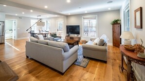 A spacious living room with a large sofa, a smaller sofa, a coffee table, and a TV. There is a dining area in the background with a table and chairs. - Sunsets On Blue Hill, Newly Renovated Farmhouse (Great Barrington)
