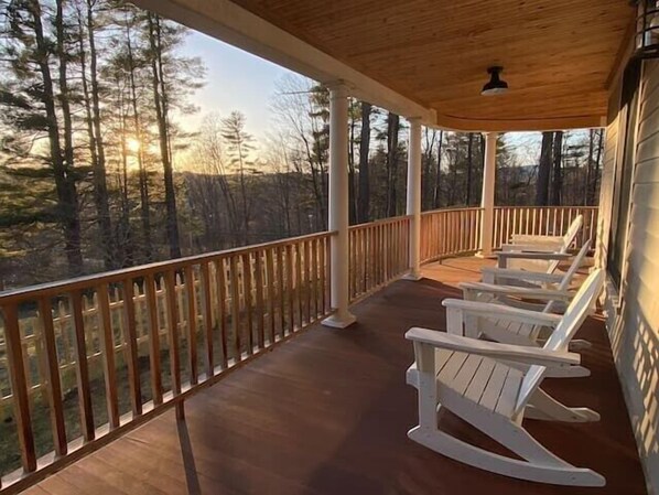 A covered porch with wooden railings and white rocking chairs, overlooking a forested area.