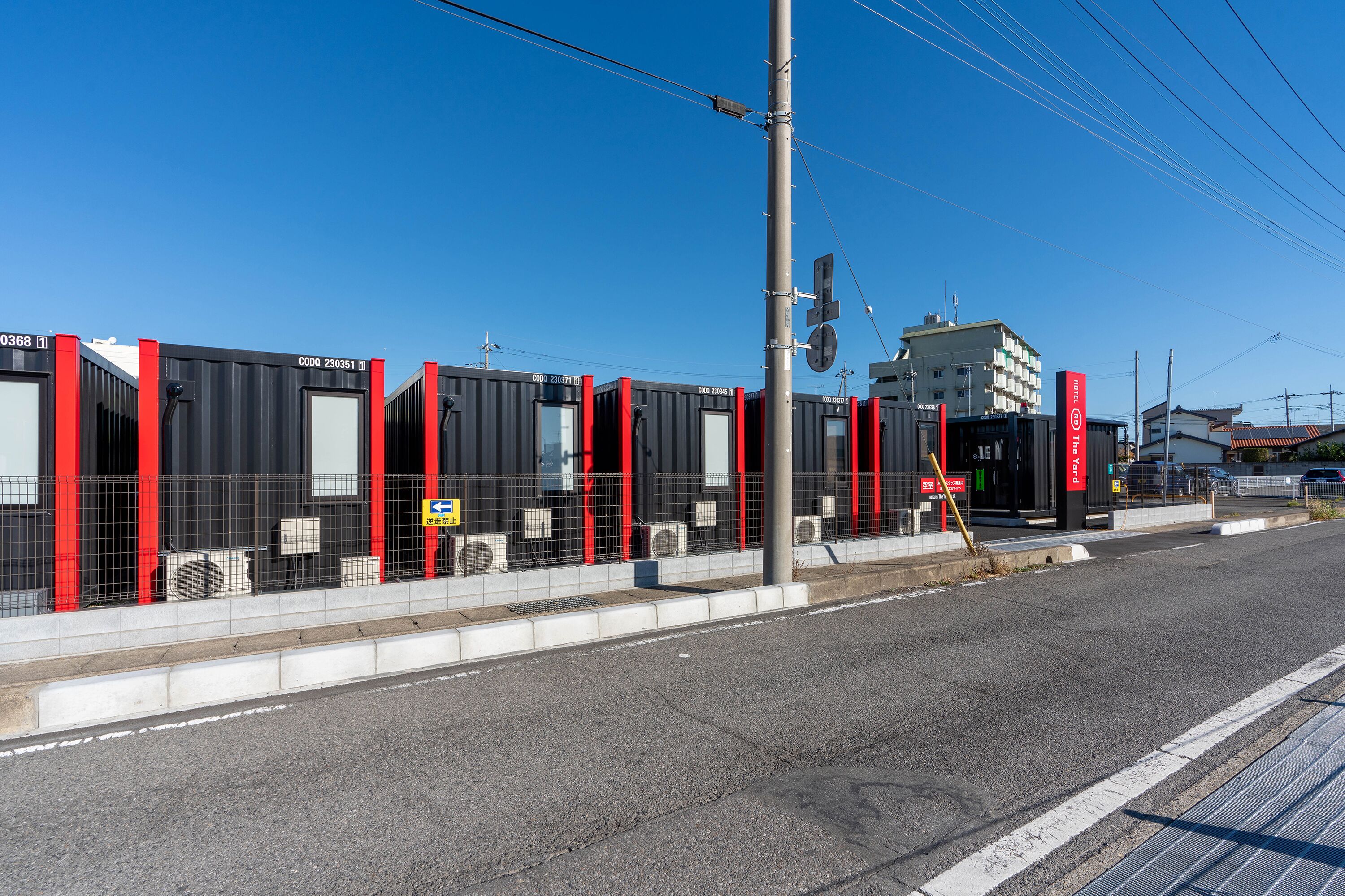 Une rangée de bâtiments modulaires noirs et rouges, avec des unités de climatisation bien visibles, et un ciel bleu dégagé.