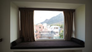 A room with a window seat overlooking a cityscape with buildings and a mountain. - Hotel Seasons (Tiruvannamalai)