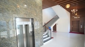 A modern interior with a marble wall, a staircase, and a chandelier. - Hotel Seasons (Tiruvannamalai)