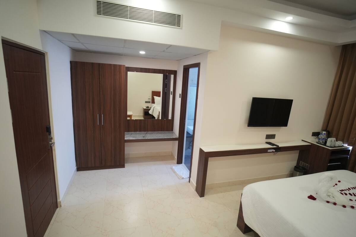 Quarto de hotel com uma cama, uma escrivaninha, televisão e guarda-roupa.