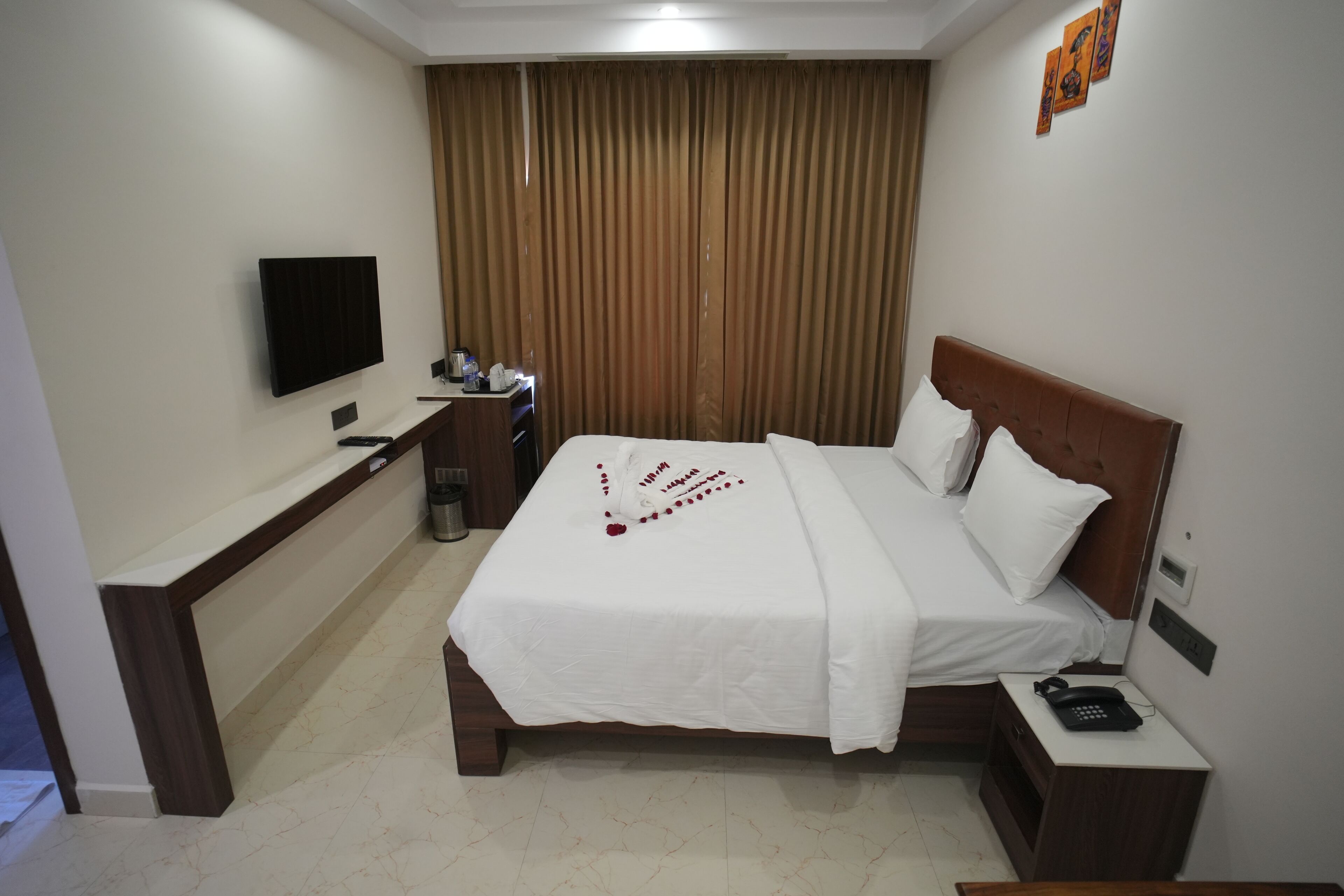 A hotel room with a bed, bedside table, TV, and a desk with a chair.