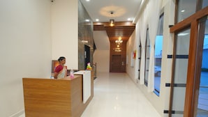 A hotel reception area with a wooden reception desk, a receptionist, and a staircase leading to the upper floor. - Hotel Seasons (Tiruvannamalai)