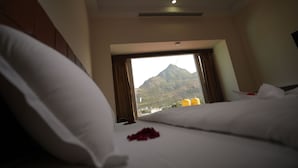 A hotel room with a bed, pillows, and a window with a mountain view. - Hotel Seasons (Tiruvannamalai)