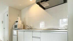 A modern kitchen with white cabinetry, a microwave, a refrigerator, and a stainless steel range hood. - Lovely Studio for 6 Ppl with Very Good Location (Naka Ward, Hiroshima)
