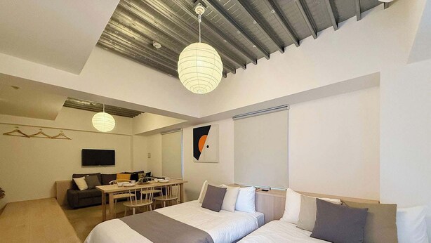 A modern hotel room with two large beds, a desk with chairs, a flat-screen TV, and a ceiling light fixture. - Lovely Studio for 6 Ppl with Very Good Location (Naka Ward, Hiroshima)