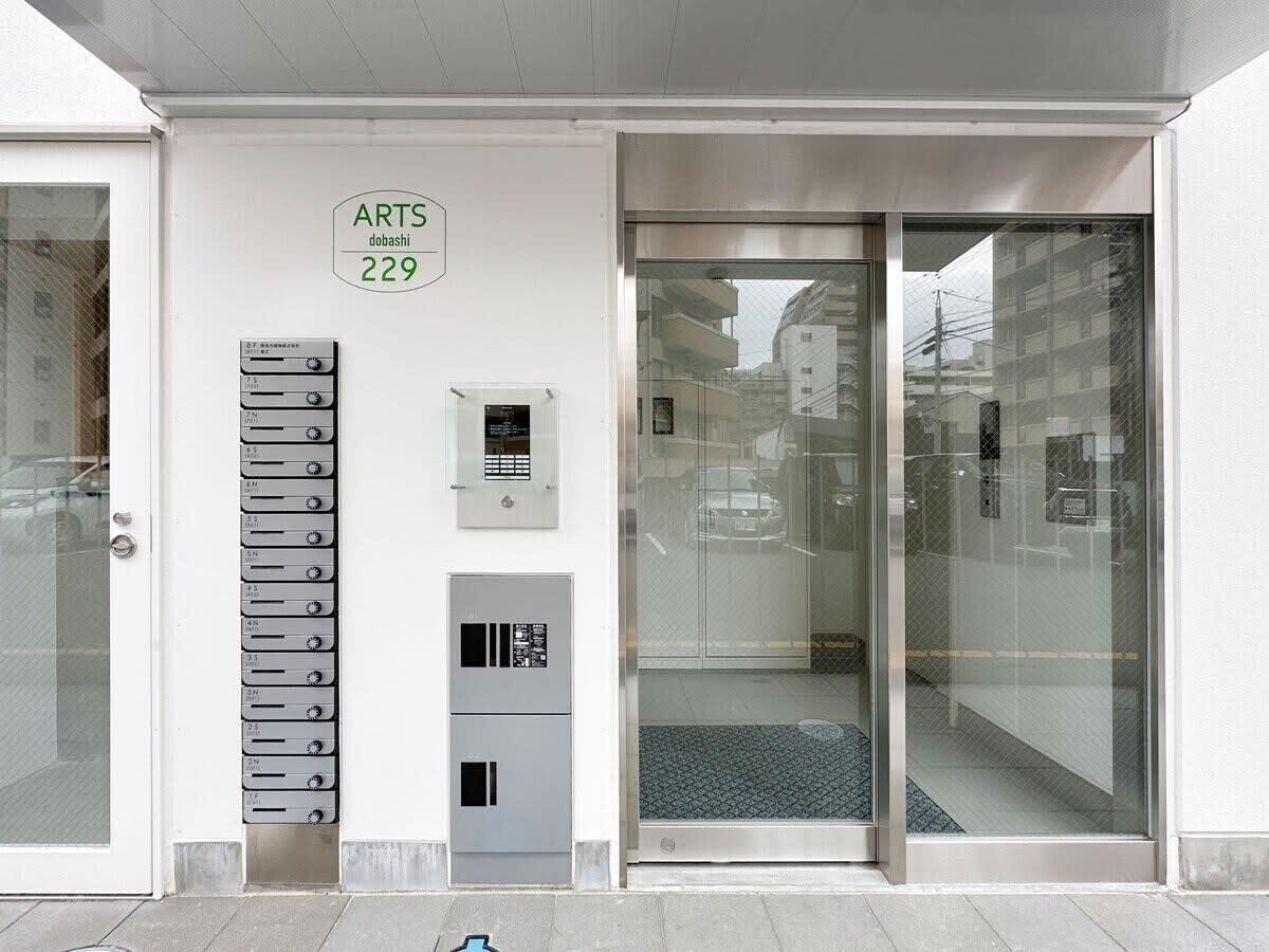 Entrada de un edificio con puerta de vidrio, un letrero que dice "ARTS 229" y un conjunto de buzones.
