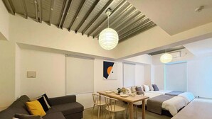 A modern living space with a sectional sofa, a dining table, and a bed. - Lovely Studio for 6 Ppl with Very Good Location (Naka Ward, Hiroshima)