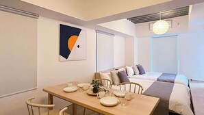 A modern, compact room with a dining table set for four, a sofa bed, and a large abstract painting on the wall. - Lovely Studio for 6 Ppl with Very Good Location (Naka Ward, Hiroshima)