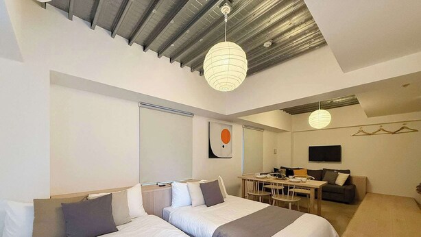 A modern hotel room with two beds, a dining area, and a TV. - Beautiful Apt in the Heart of the City (Naka Ward, Hiroshima)