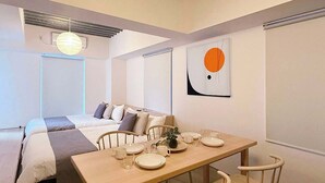 A modern, minimalist room with a wooden dining table set for two, a bed with a gray and white striped bedspread, and a large abstract painting on the wall. - Beautiful Apt in the Heart of the City (Naka Ward, Hiroshima)