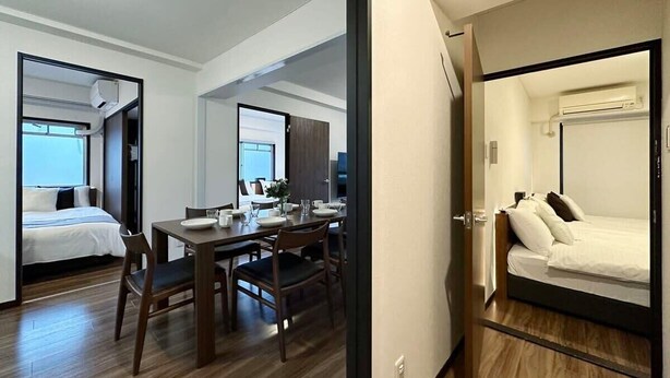 A hotel room with a bed, a dining table with chairs, and a separate bedroom area. - Apt for 14 Ppl Great Location In a Quiet Area (Naka Ward, Hiroshima)