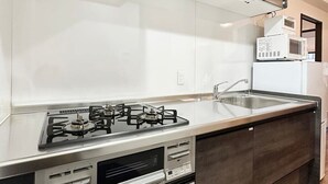 A modern kitchen with a gas stove, stainless steel countertops, dark cabinetry, and a built-in microwave. - Apt for 14 Ppl Great Location In a Quiet Area (Naka Ward, Hiroshima)