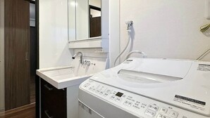 A compact hotel bathroom with a sink, mirror, and a front-loading washing machine. - Apt for 14 Ppl Great Location In a Quiet Area (Naka Ward, Hiroshima)