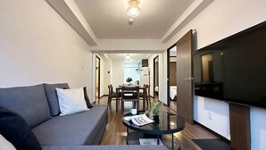 A modern living room with a sofa, a coffee table, and a TV. There is a dining area with a table and chairs in the background. - Apt for 14 Ppl Great Location In a Quiet Area (Naka Ward, Hiroshima)