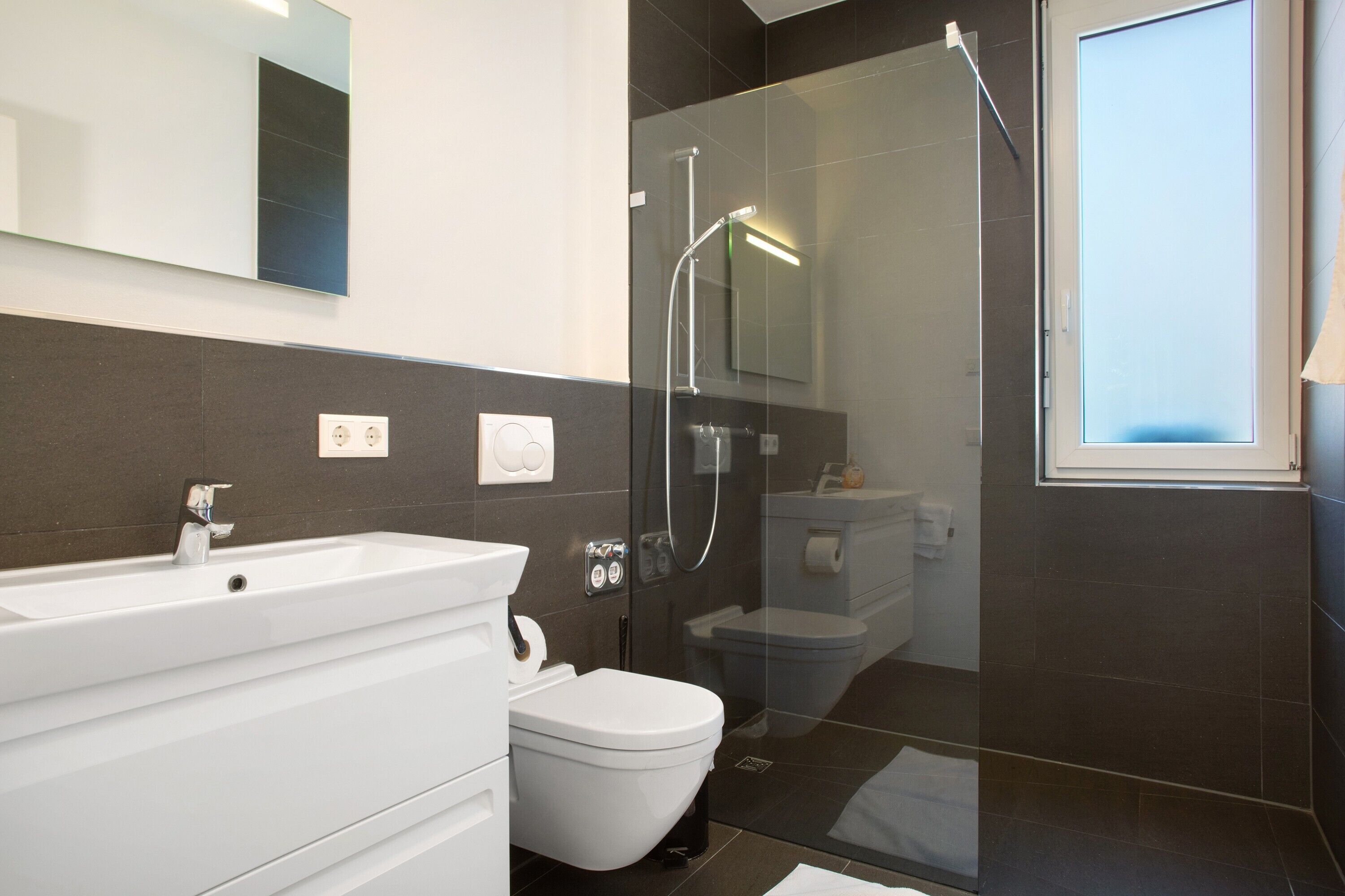 Ein modernes Badezimmer mit einer Duschkabine aus Glas, einem weißen Waschbecken und einer Toilette.