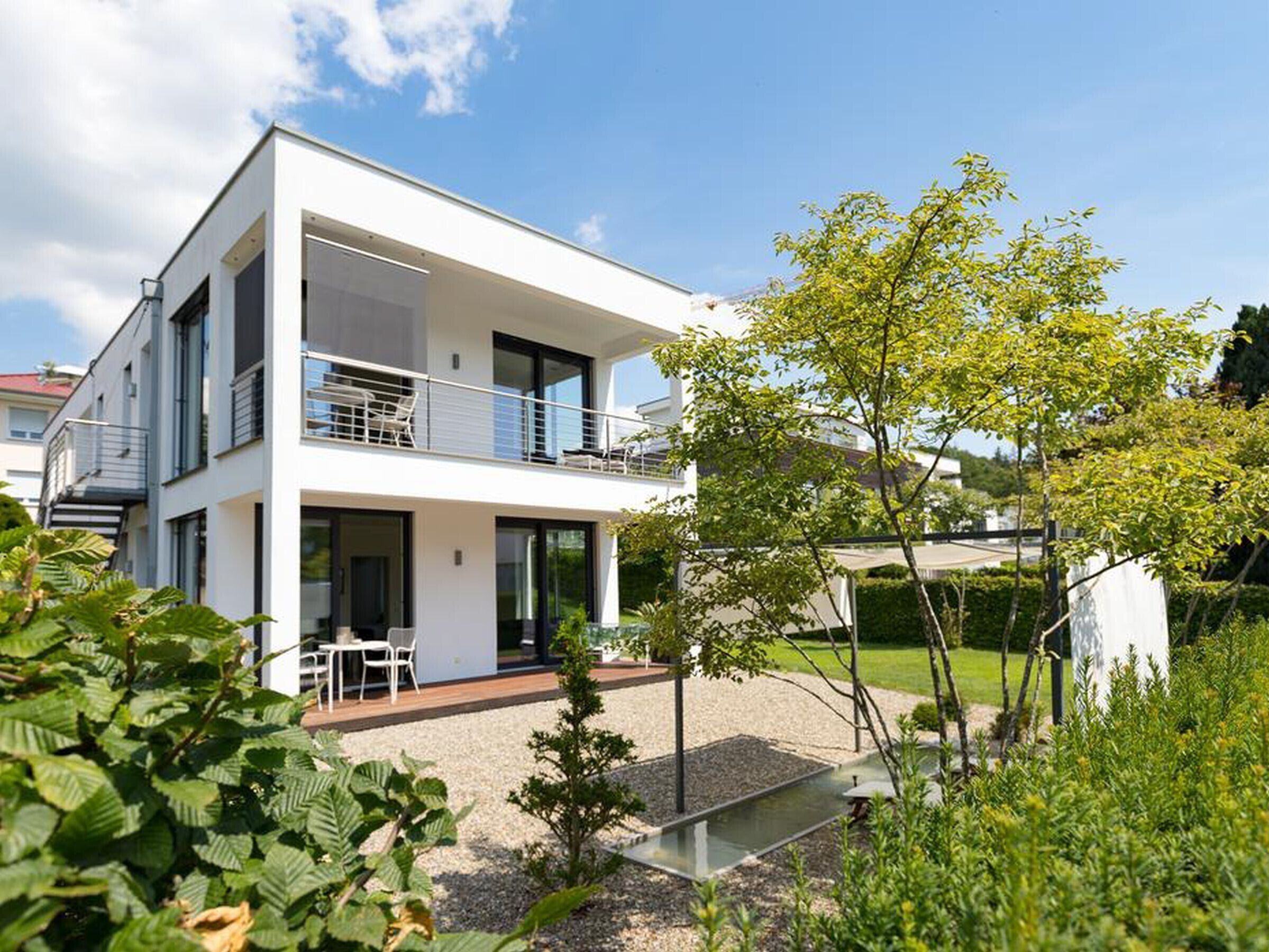 Ein modernes, zweistöckiges Haus mit Balkon, Garten und blauem Himmel.