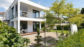 Et moderne hus med to etager, en altan, en have og en klar himmel.