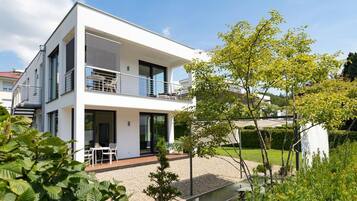 Ein modernes, zweistöckiges Haus mit Balkon, Garten und blauem Himmel.