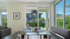 Et moderne spiseområde med et glasbord, to stole, en bænk og en hængende lampe.