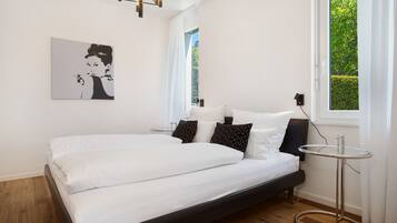 Ein modernes Schlafzimmer mit Bett, Nachttisch, Wandleuchte, einem Fenster mit Vorhängen und einem gerahmten Bild an der Wand.