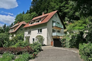 Une maison à deux étages avec un toit en pente, un balcon à l’étage supérieur et une allée menant à la porte d’entrée.