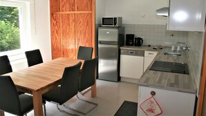 Une cuisine compacte comprenant une table à manger en bois, des chaises, un réfrigérateur, un four à micro-ondes et une machine à café.