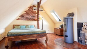 Une chambre avec un plafond en pente, un lit en bois, un radiateur encastré et un escalier en briques.
