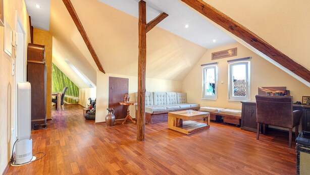 Un loft spacieux avec de hauts plafonds, des poutres apparentes, une grande fenêtre et un coin salon confortable.