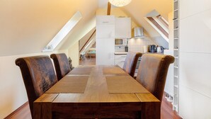 Un coin repas avec une table et des chaises en bois, une cuisine à l’arrière-plan et un plafond en pente agrémenté d’un luminaire.