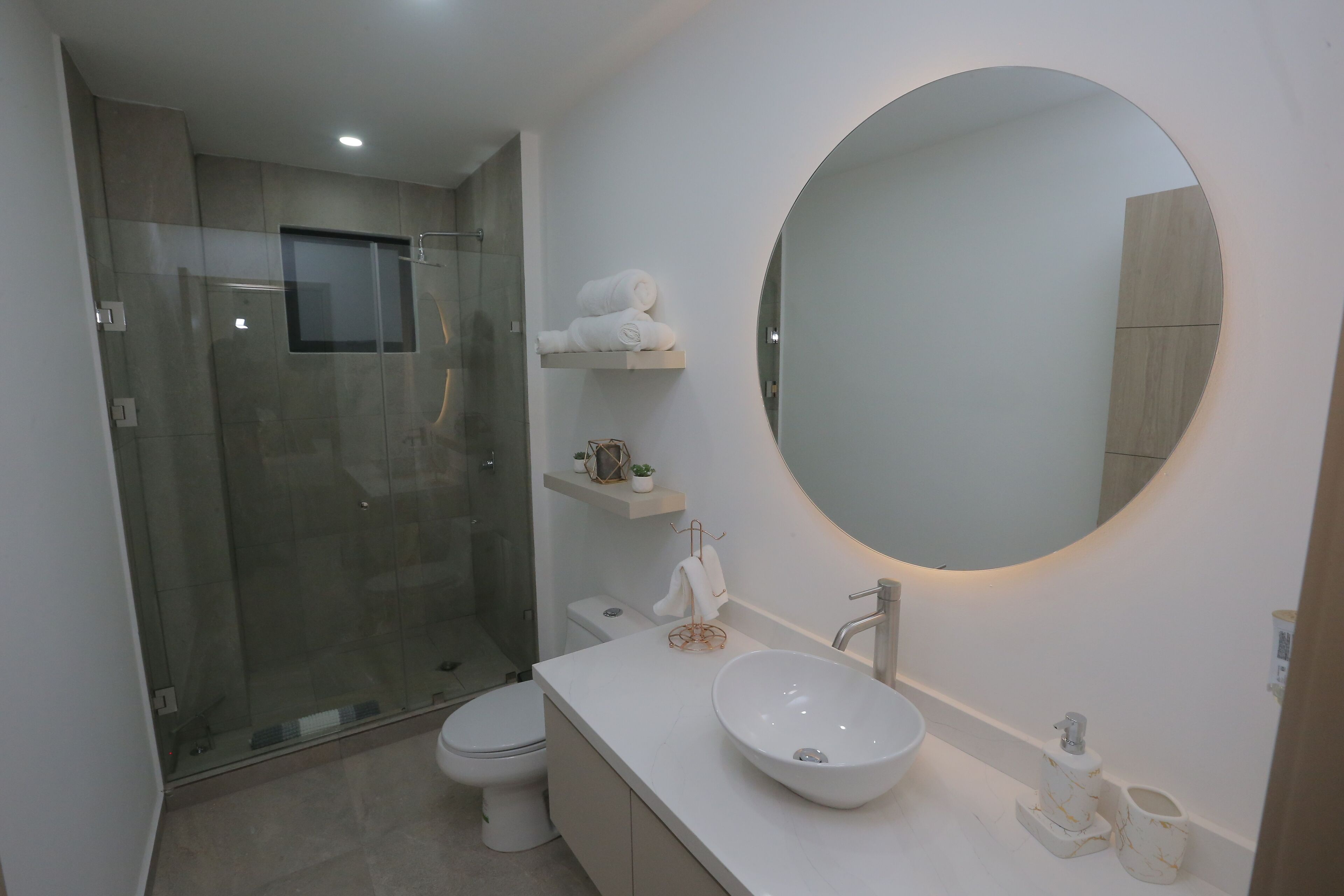 A modern bathroom with a glass-enclosed shower, a white sink, and a large mirror.