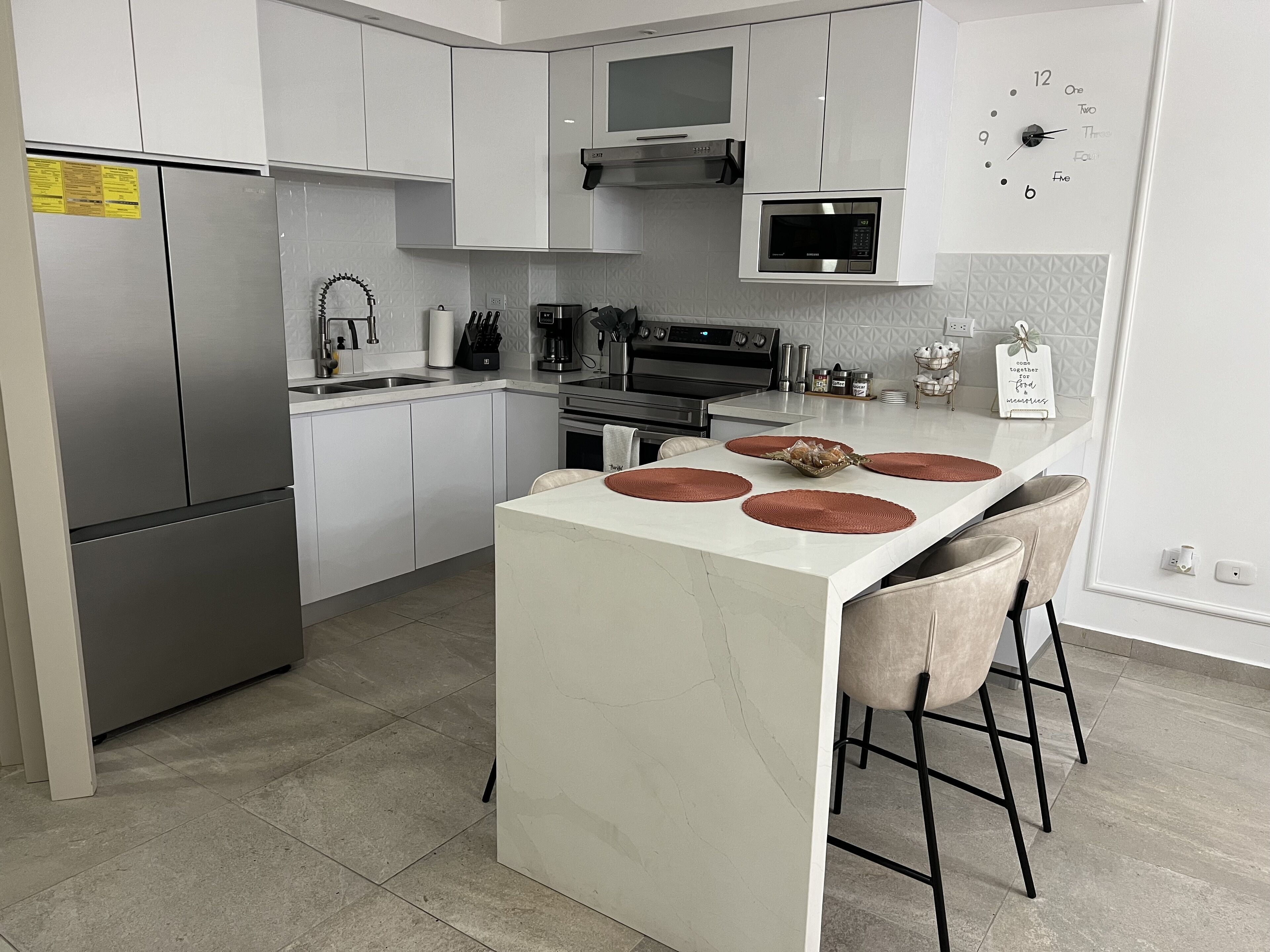 Una cocina moderna con gabinetes blancos, electrodomésticos de acero inoxidable y una isla central con taburetes.