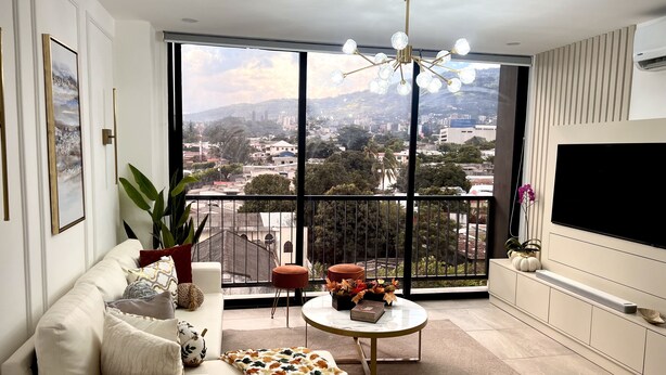 A spacious living room with a large window, a sofa, a coffee table, and a flat-screen TV.