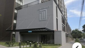 A modern building with a grey facade, the word "CONDOMINIO" prominently displayed, and a covered entrance area with small plants.