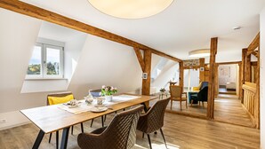 Uma sala de jantar com uma mesa de madeira, cadeiras e vista para o exterior.