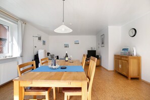 A dining area with a wooden table, chairs, a blue table runner, a hanging light fixture, and a wooden cabinet.