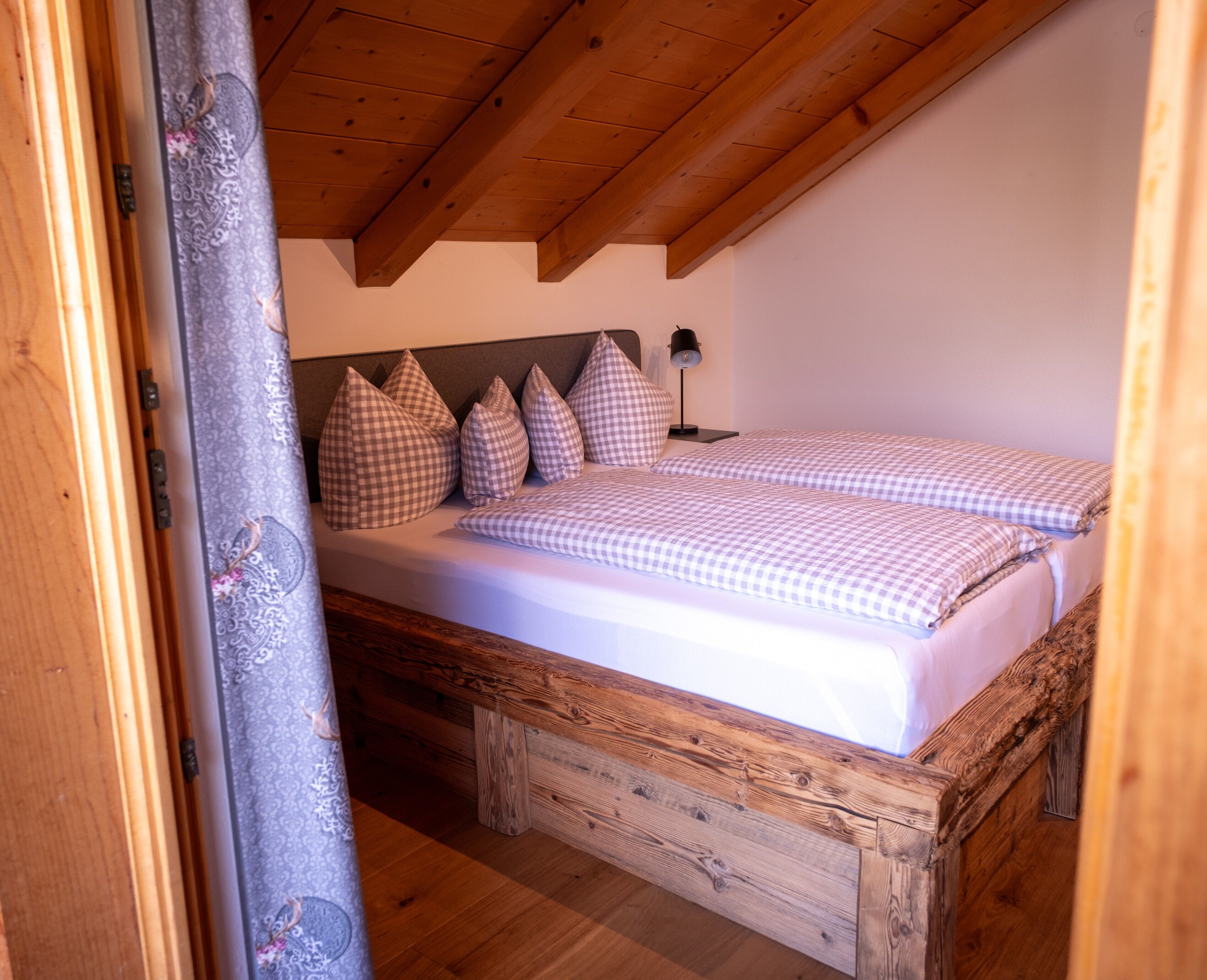 Een slaapkamer met een houten bed, geruit beddengoed en een hoofdbord met meerdere kussens.
