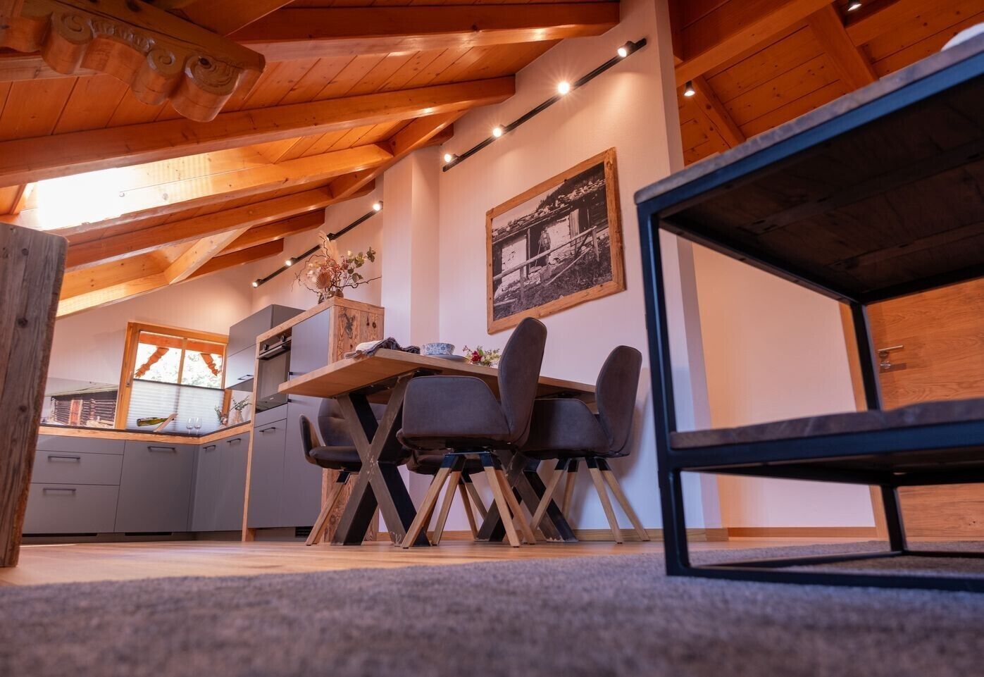 Un comedor acogedor con una mesa y sillas de madera, una cocina al fondo y un cuadro en la pared.