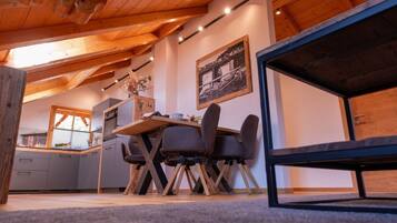 Un comedor acogedor con una mesa y sillas de madera, una cocina al fondo y un cuadro en la pared.