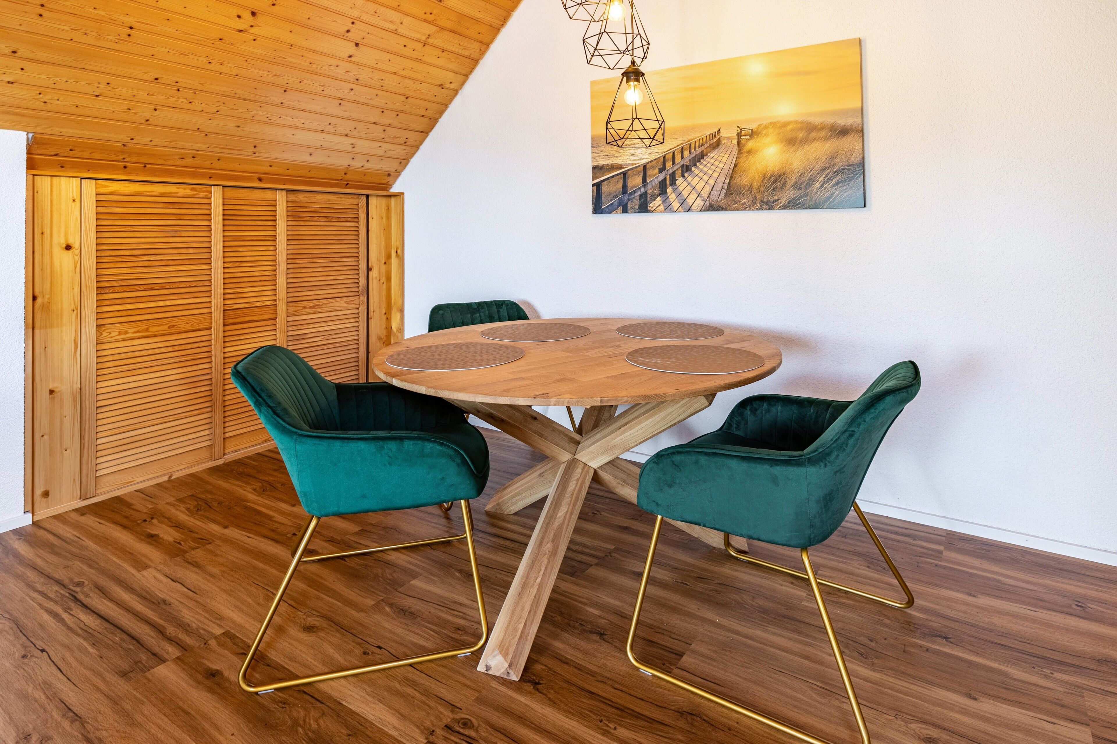 Un comedor con una mesa redonda de madera, cuatro sillas de terciopelo verde y techo de madera.