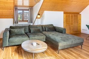 A modern living room with a sectional sofa, a round coffee table, a floor lamp, and a view of the outside through a window. - Apartment 'Anne' with Lake View, Balcony and Wi-Fi (Öhningen)