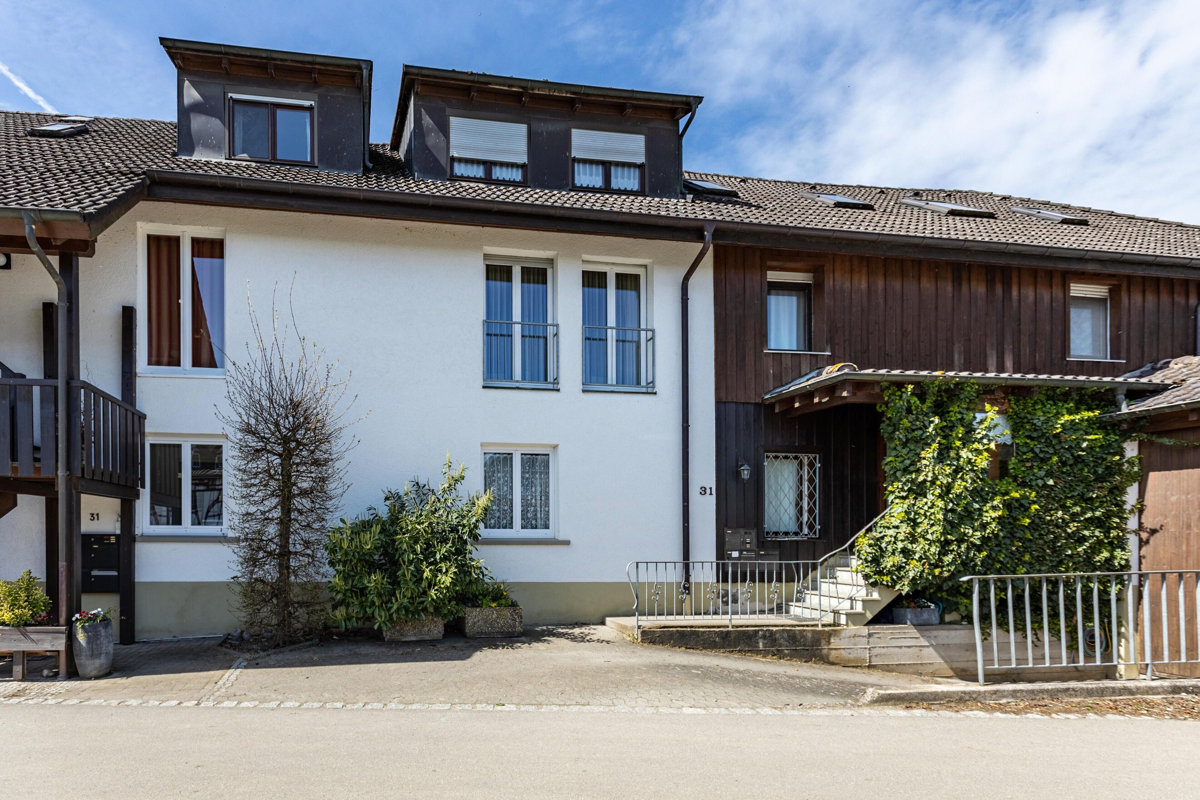 Un immeuble résidentiel de deux étages doté d’un balcon, d’un petit jardin et d’un escalier menant à l’entrée.