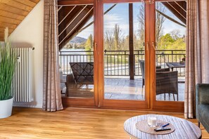A room with a wooden floor, a round table with a remote control, a glass of milk, and a potted plant. - Apartment 'Anne' with Lake View, Balcony and Wi-Fi (Öhningen)
