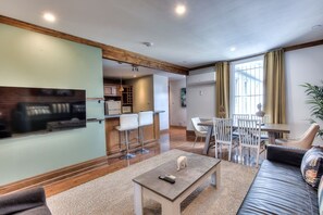 Una sala de estar moderna con un televisor de pantalla plana, una zona de comedor con sillas y una cocina al fondo.